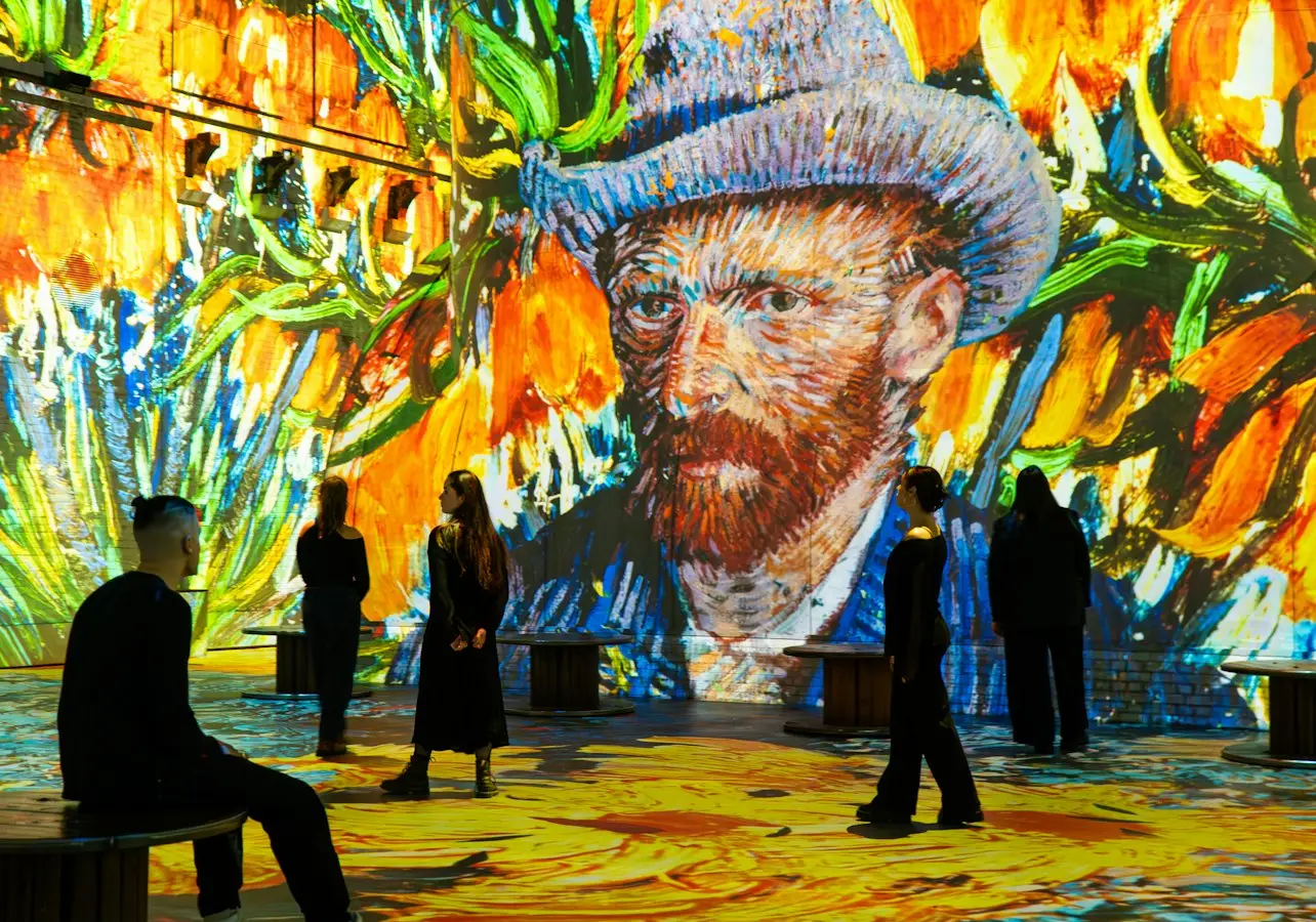 People observing a digital Van Gogh art installation with vibrant colors and large floral projections on the walls and floor.